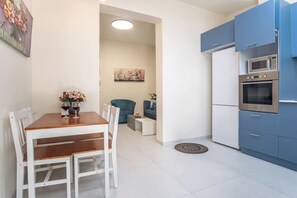 A modern kitchen with blue cabinets, a built-in oven, and a dining area with a wooden table and white chairs. - Port city haifa - 1 bdrm apt Near beach 2 (Haifa)
