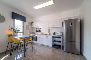 Eine moderne Küche mit weißen Schränken, einem Edelstahl-Kühlschrank und einem Essbereich mit gelben Stühlen.