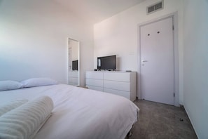 Ein Schlafzimmer mit Bett, Kommode, Fernseher und einer Tür.