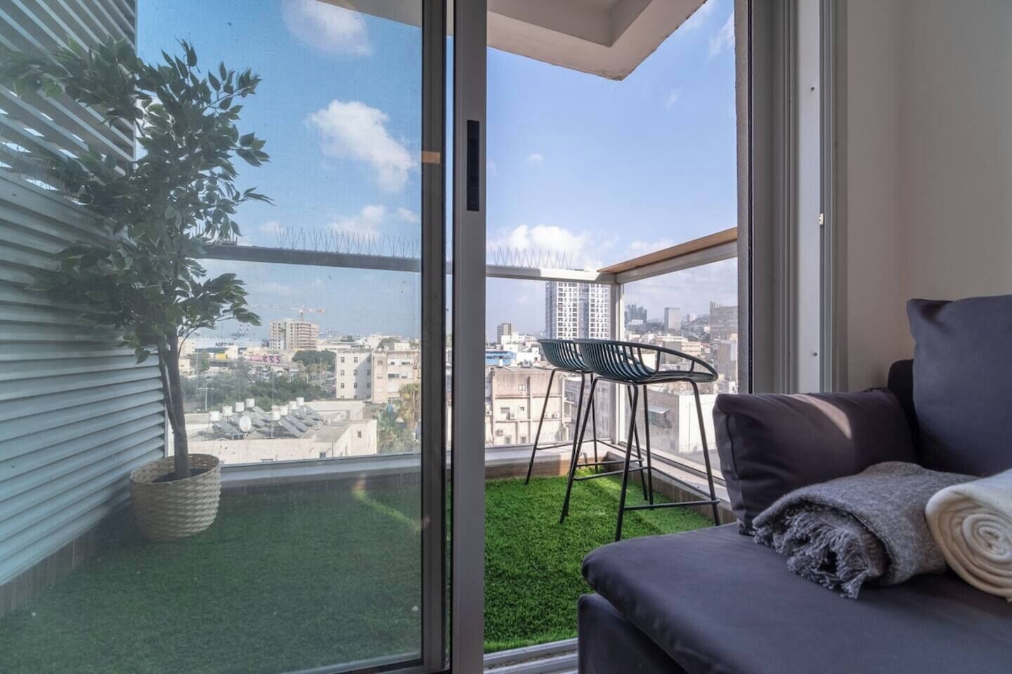 A balcony with a view of a cityscape, a potted plant, a chair, and a sofa.