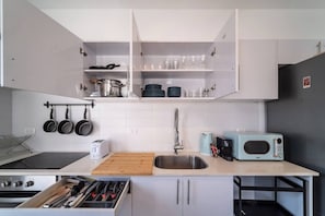 Eine moderne Küche mit weißen Schränken, einer Edelstahlspüle, einem Toaster, einer Mikrowelle und hängenden Töpfen.