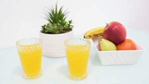 Zwei Gläser Orangensaft, ein Blumentopf und eine Obstschale mit Äpfeln, Birnen und Orangen.