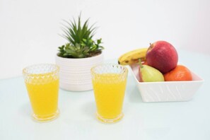 Two glasses of orange juice, a potted plant, and a bowl of fruit including apples, pears, and oranges. - Port city-german colony 2 bdrms w/balcony+mamad 1 (Haifa)