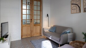 A modern living room with a grey sofa, a wooden door, a television, and patterned floor tiles. - Huys17 (Hasselt)