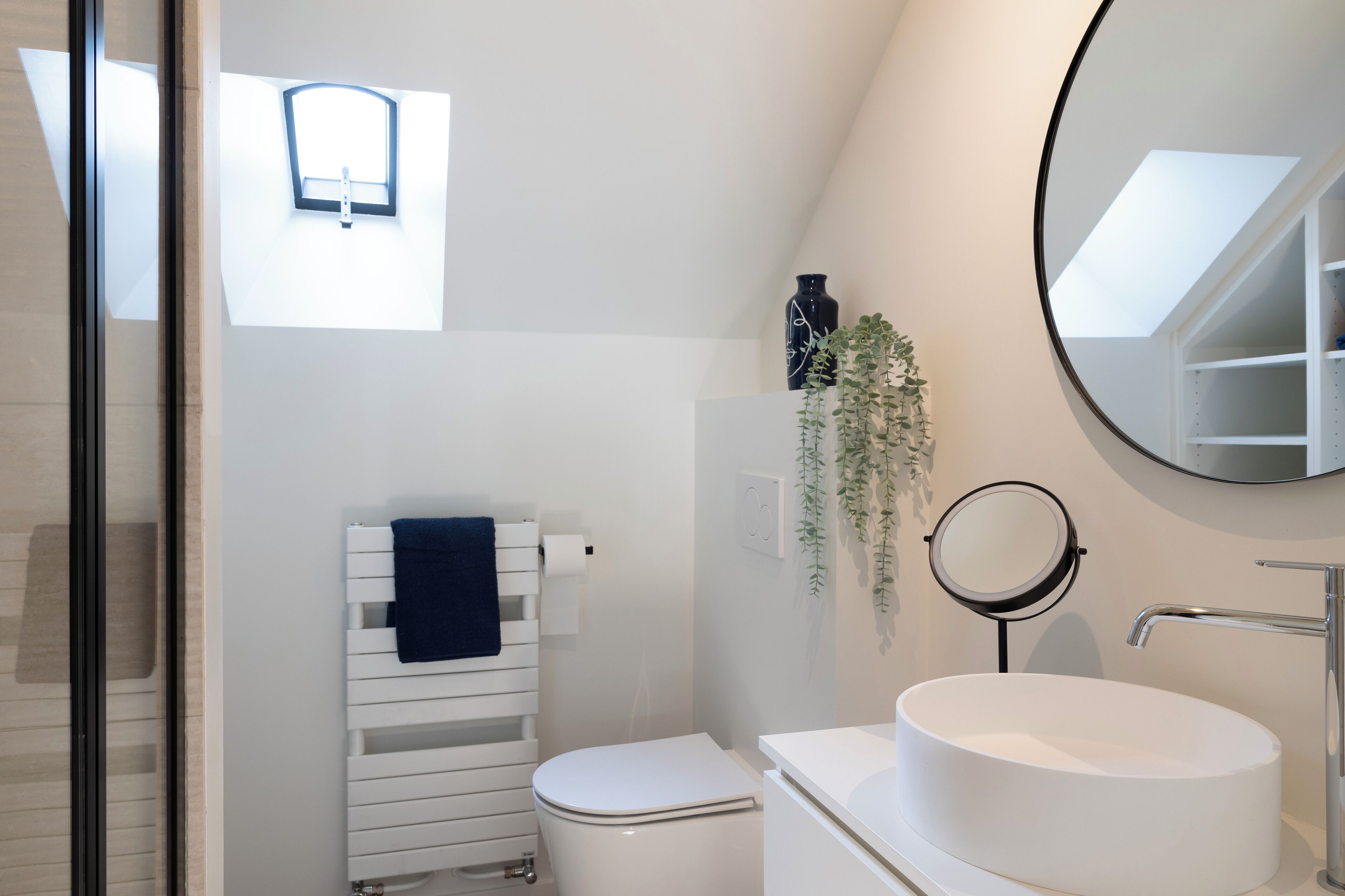 A modern bathroom with a white toilet, a round mirror, and a white sink.