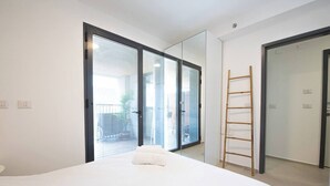 Een slaapkamer met een bed, een schuifglazen deur, een houten ladder en een witte muur.