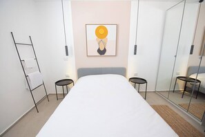 A modern hotel room with a large bed, two bedside tables, a towel rack, a painting on the wall, and a glass partition. - Haifa German Colony 2BR, Balcony & Port View (Haifa)