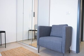 Habitació moderna amb una poltrona tapissada de color gris, una taula petita negra i una paret divisòria de vidre.