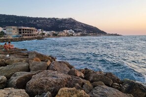 A coastal scene with rocky terrain and a building complex in the background. - Port city- 1 bdrm apt w/ balcony beachfront+ mamak (Haifa)