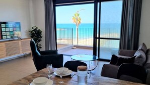A dining area with a table set for two, a sofa, and a view of the ocean through large windows. - Port city- 1 bdrm apt w/ balcony beachfront+ mamad (Haifa)