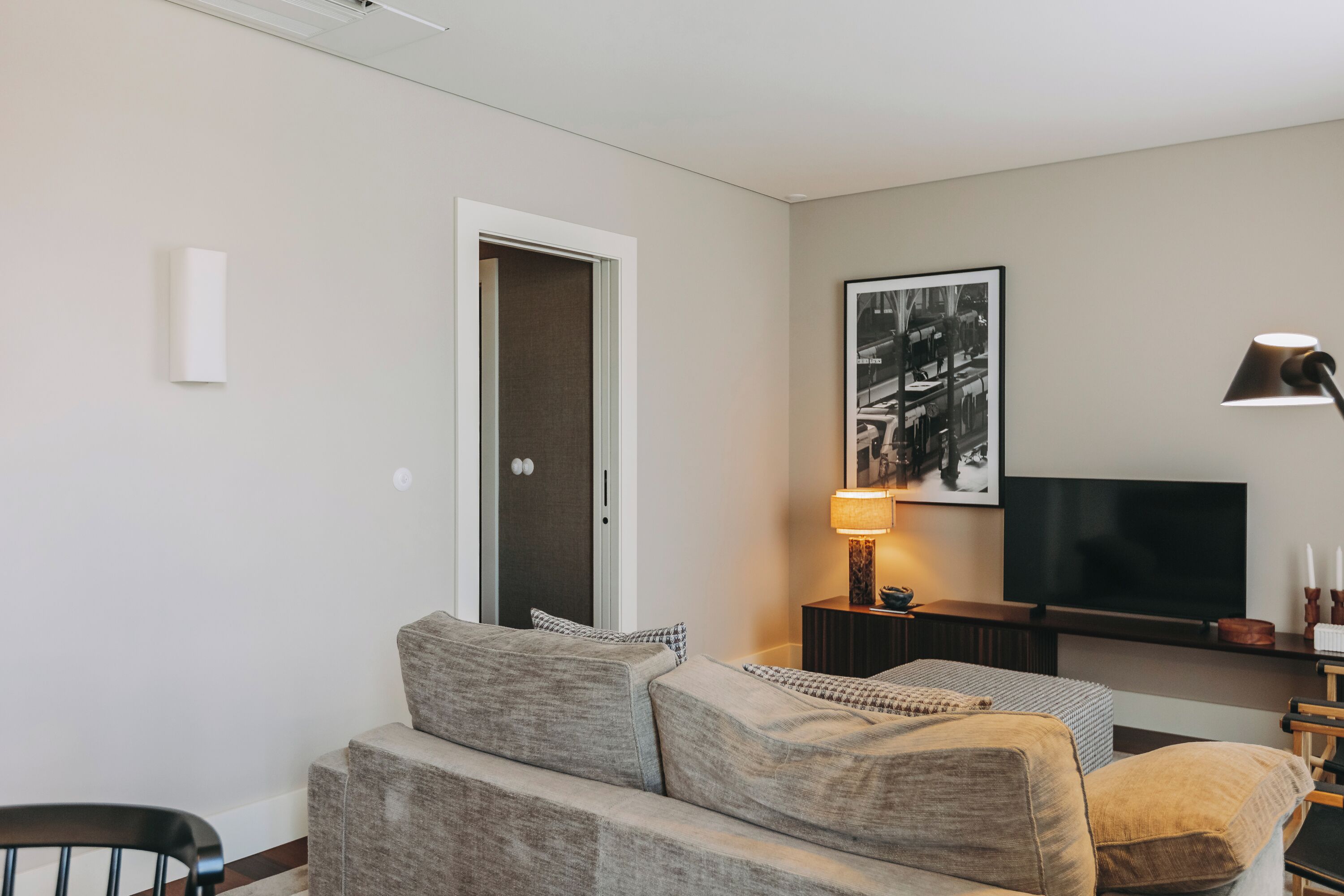 A modern living room with a grey sofa, a flat-screen TV, a lamp, and a framed picture on the wall.