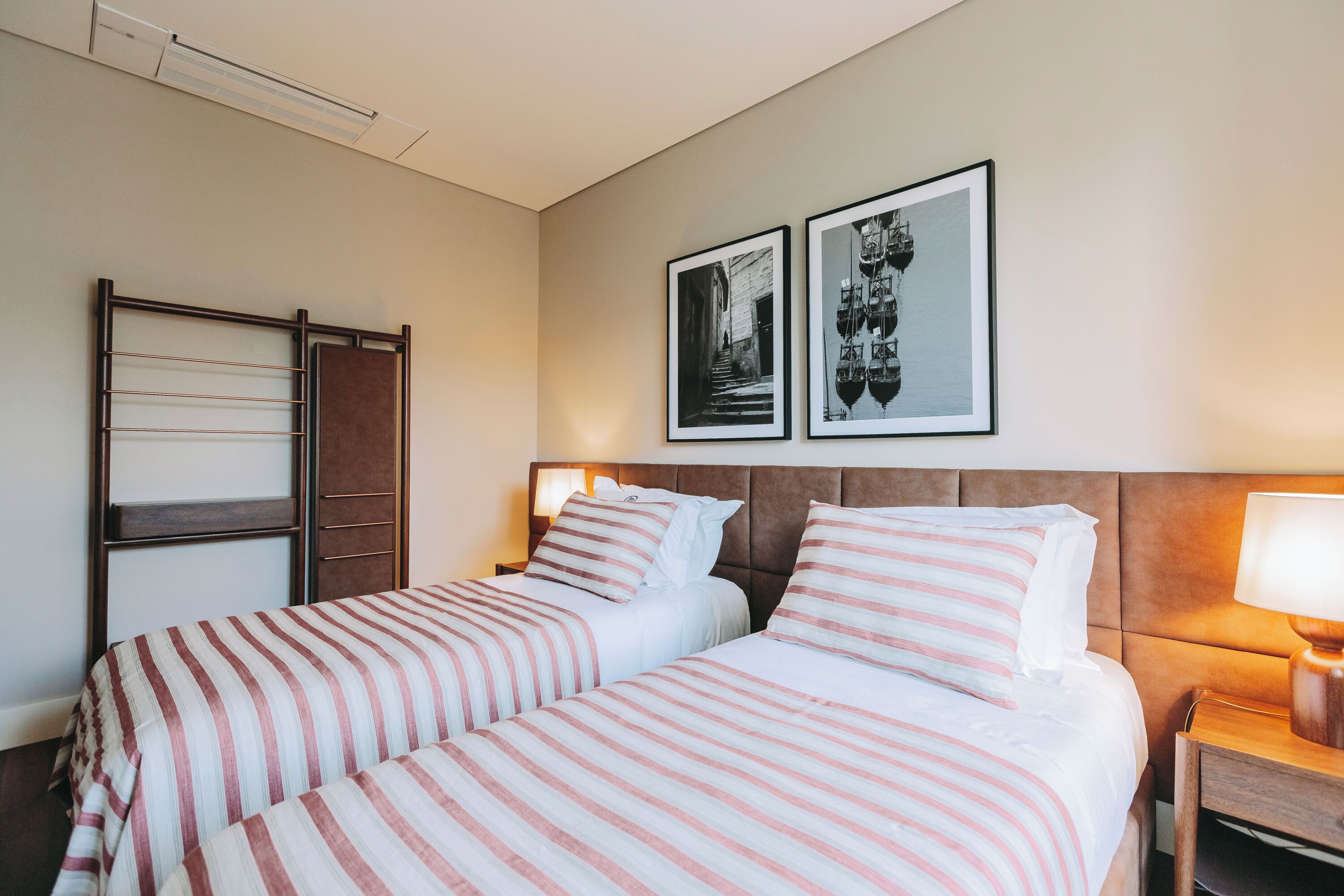 Ein Hotelzimmer mit zwei Betten, einem Kopfteil, einem Nachttisch und zwei gerahmten Bildern an der Wand.