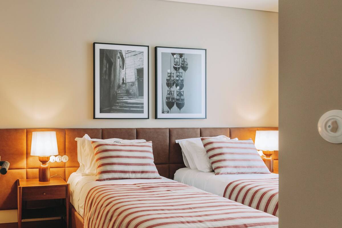 Hotelkamer met twee bedden, een nachtkastje met lamp en twee ingelijste foto’s aan de muur.