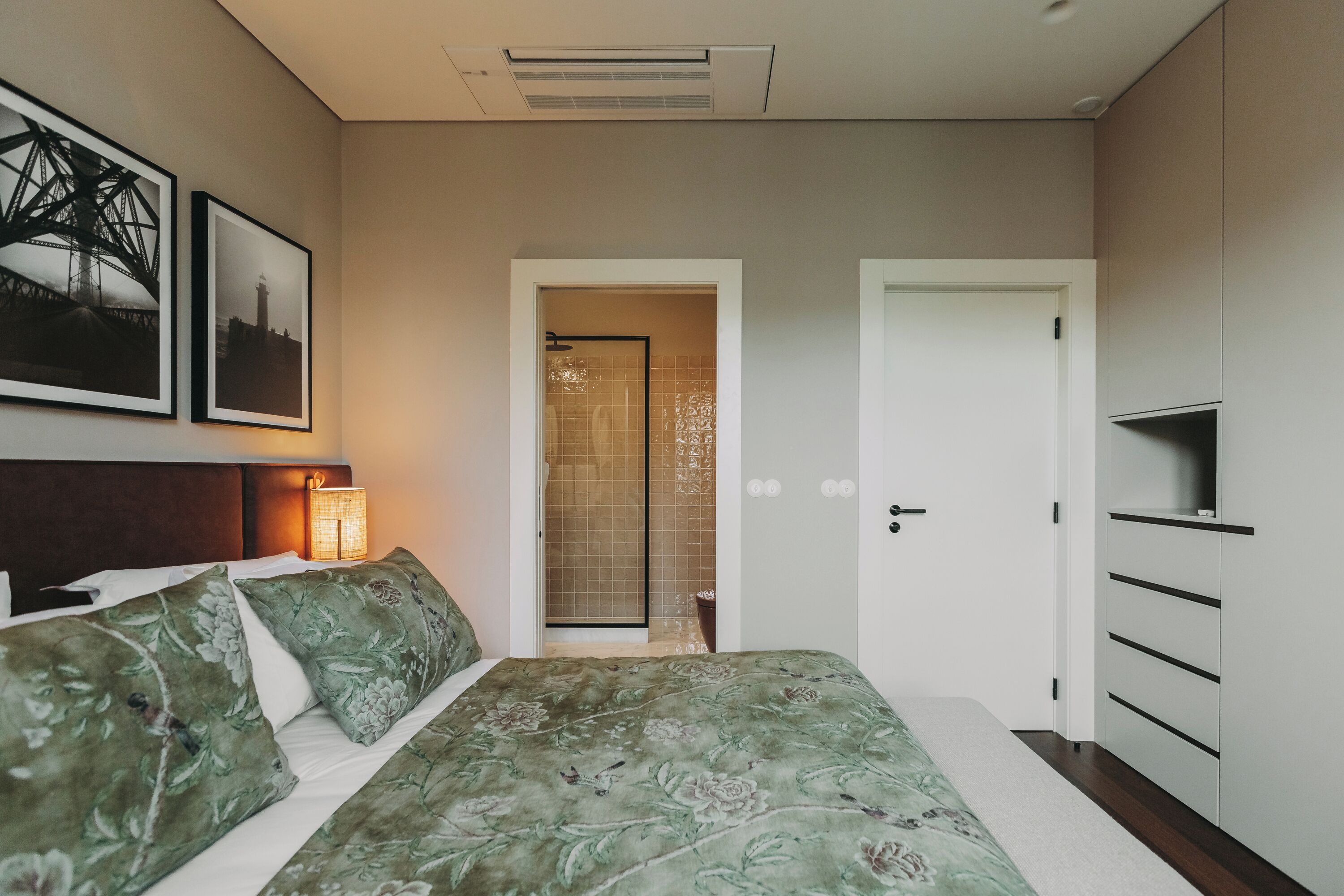 Une chambre à coucher comprenant un lit, une table de chevet, une lampe, une armoire et une porte donnant sur une salle de bain.