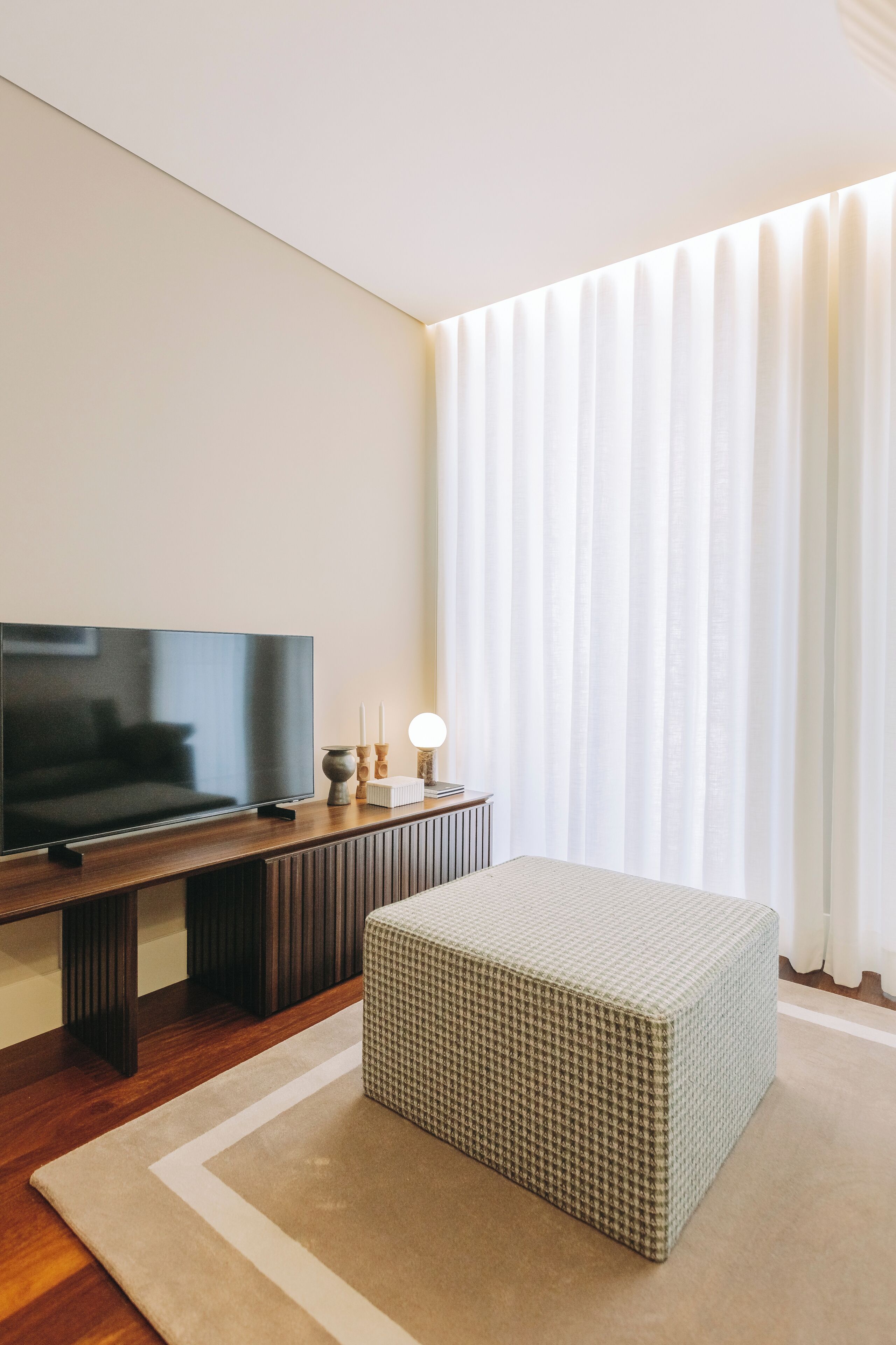 A modern living room with a flat-screen TV, a wooden coffee table, and a patterned ottoman.