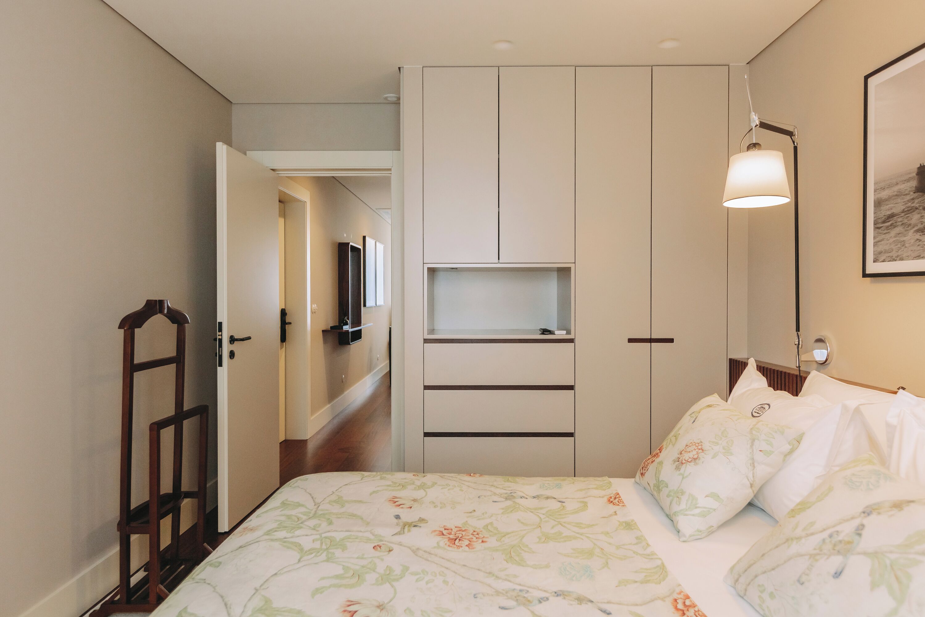 A bedroom with a bed, a wardrobe, a bedside table, a lamp, and a framed picture on the wall.