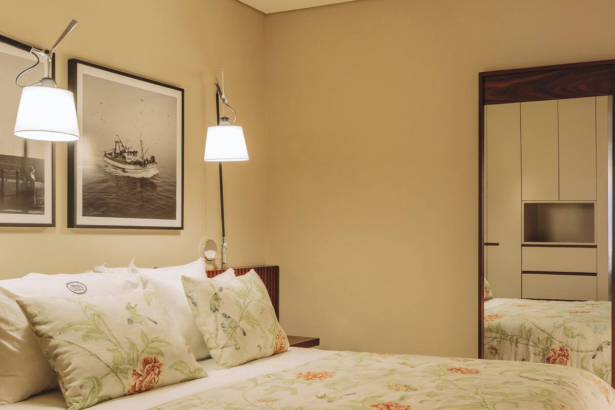 Een slaapkamer met een bed, twee wandlampen, een lijst met een afbeelding en een spiegel.