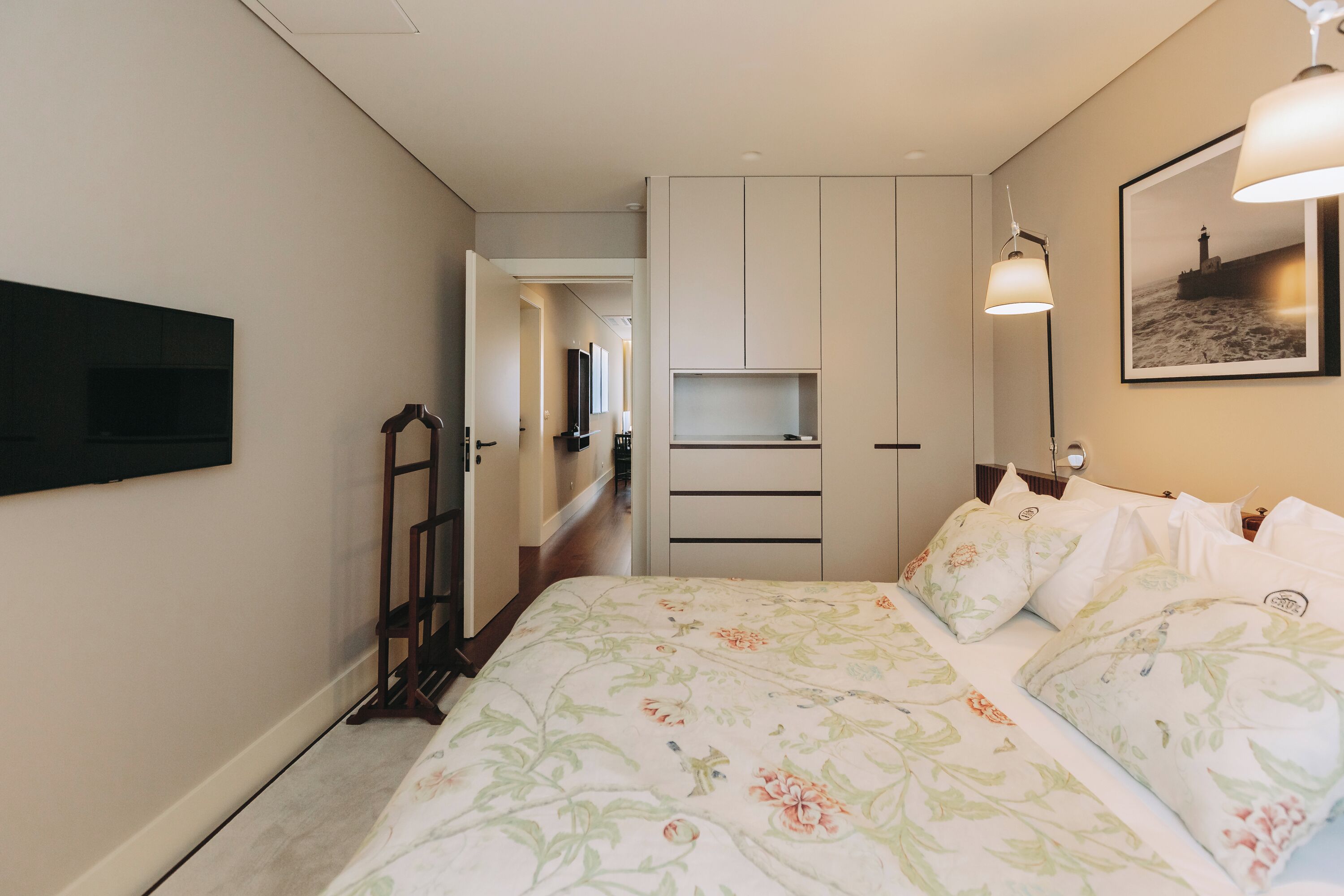 A bedroom with a bed, a wardrobe, a flat-screen TV mounted on the wall, and a framed picture on the wall.