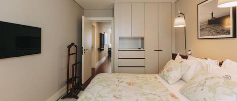 A bedroom with a bed, a wardrobe, a flat-screen TV mounted on the wall, and a framed picture on the wall.
