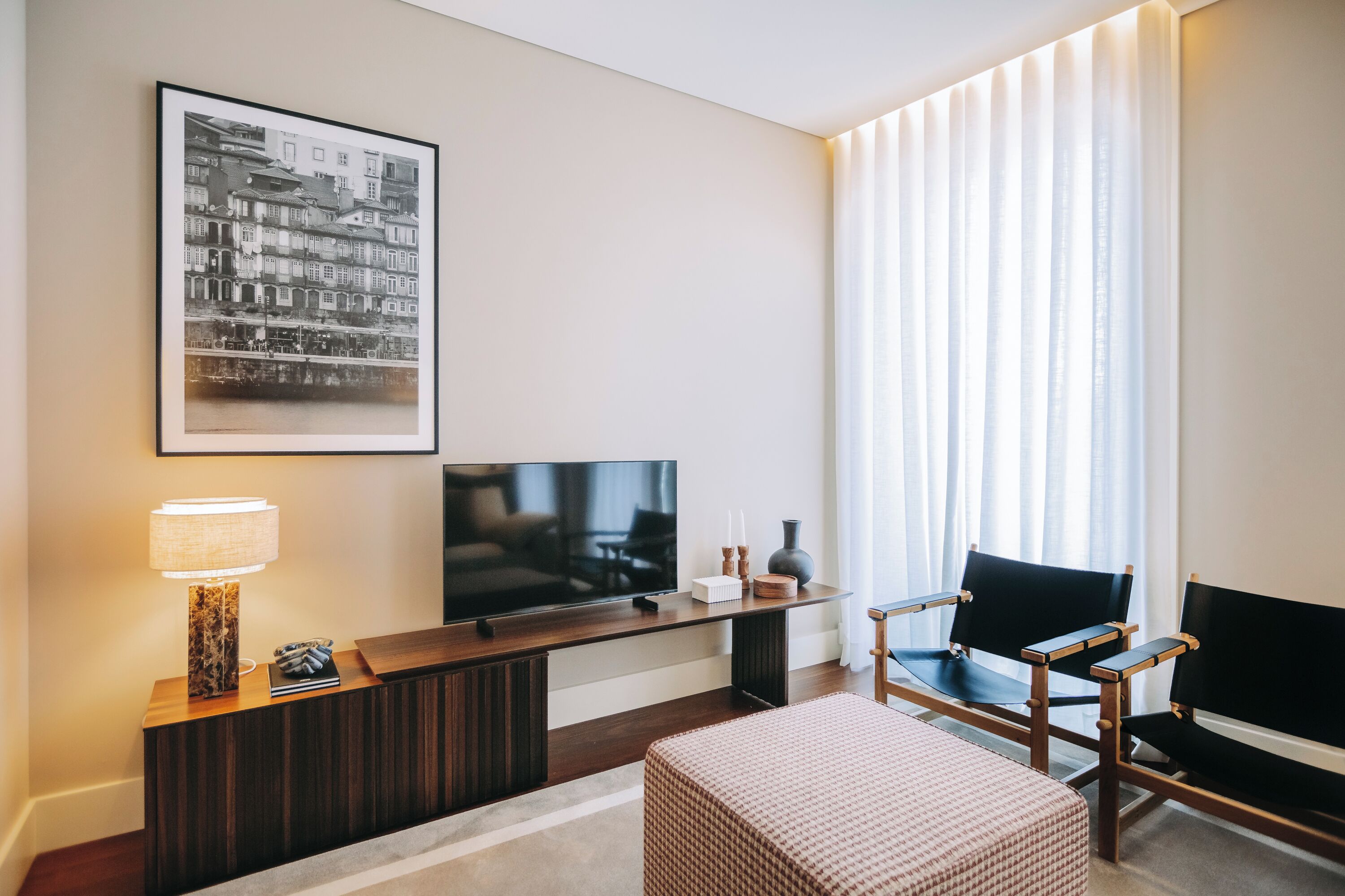 Een moderne woonkamer met een flatscreen televisie, een zwart-wit foto in een lijst, een lamp en twee stoelen.