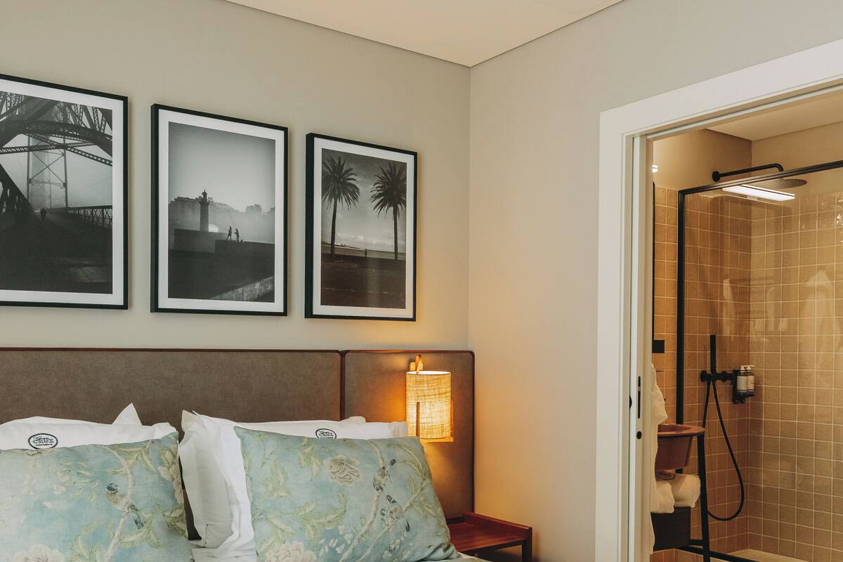 Een hotelkamer met een bed, ingelijste foto's aan de muur, een nachtkastje en een douchehoek.