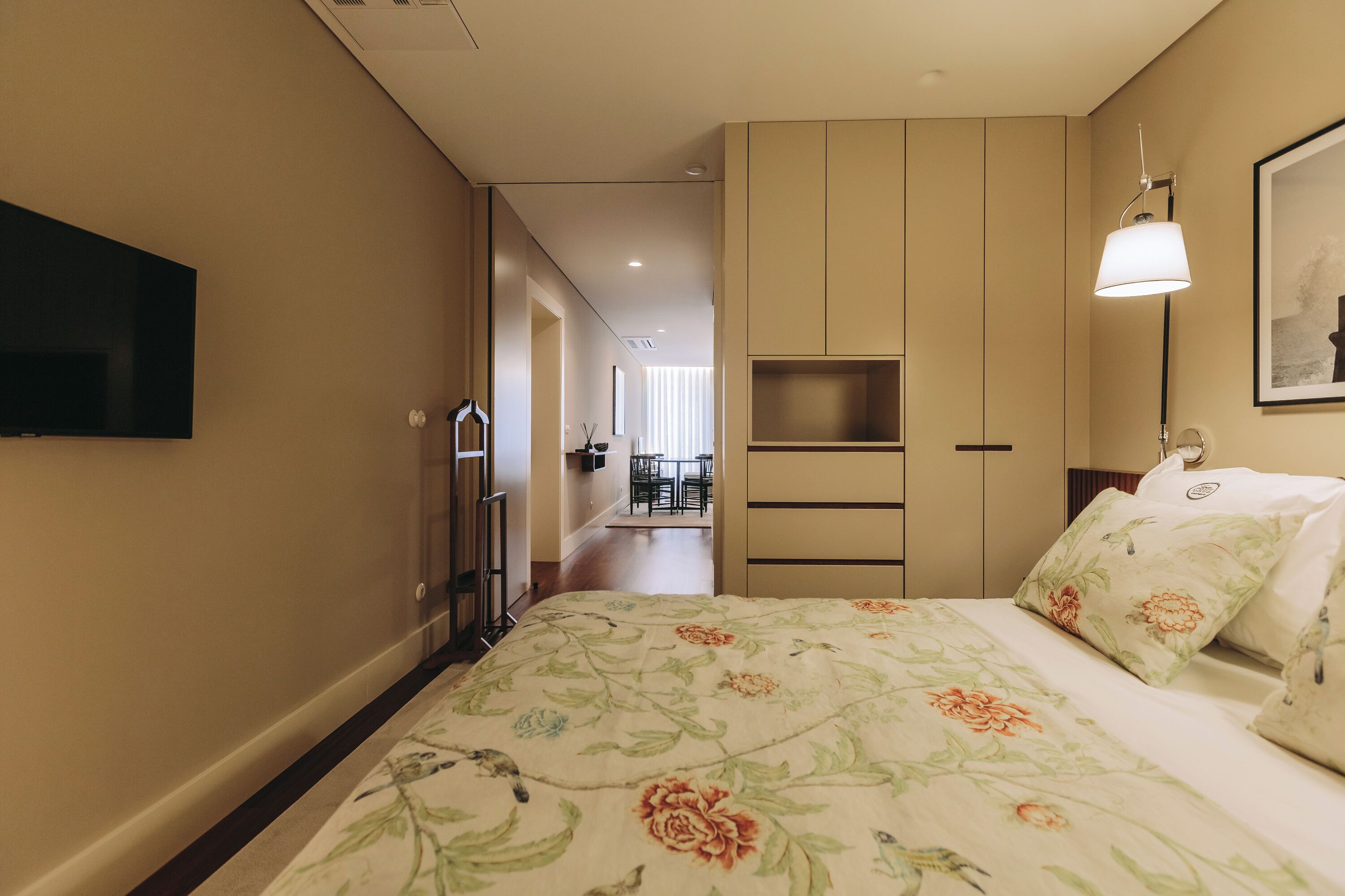 Una habitación de hotel con cama, televisión montada en la pared, escritorio y silla.
