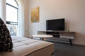 Een moderne woonkamer met een bank, een klein rond tafeltje, een flatscreen televisie en een minimalistische salontafel.
