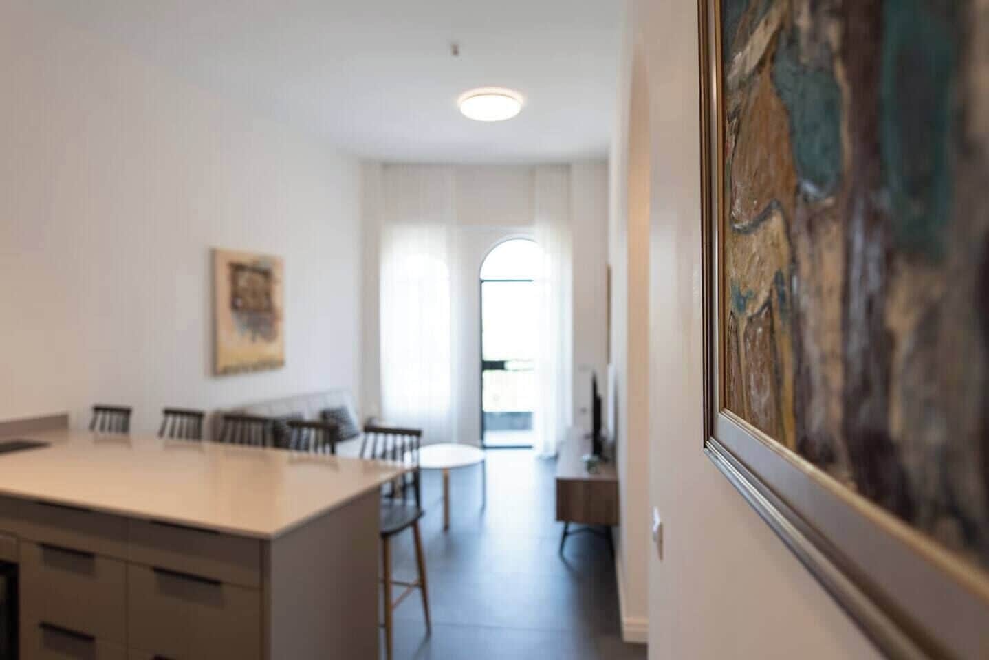 Uma cozinha moderna com ilha central, área de refeições com cadeiras e um quadro na parede.