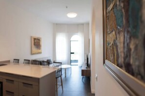 Una cuina moderna amb una illa central, menjador amb cadires i un quadre a la paret.