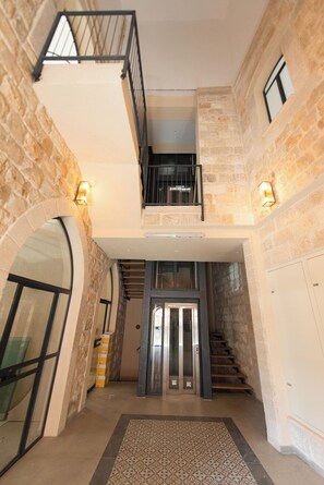 A spacious interior with a central staircase, a mezzanine level, and a stone wall. - PORT CITY - Flea Market Luxury 2 Bdrm W/ 2 Balcony (Haifa)