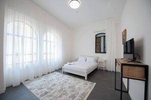 Une chambre à coucher comprenant un lit, des tables de chevet, un bureau, un téléviseur et une fenêtre avec des rideaux.