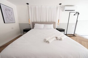 Ein Hotelzimmer mit einem großen Bett, zwei Nachttischen, einer Hängeleuchte und einem gerahmten Kunstwerk an der Wand.
