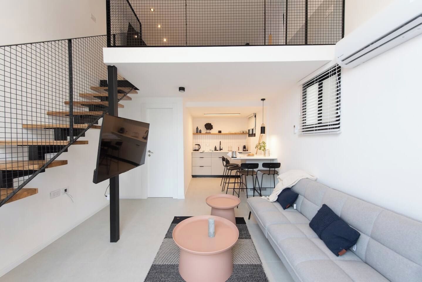 A modern apartment with a staircase, a living area with a sofa, a dining area, and a kitchen.