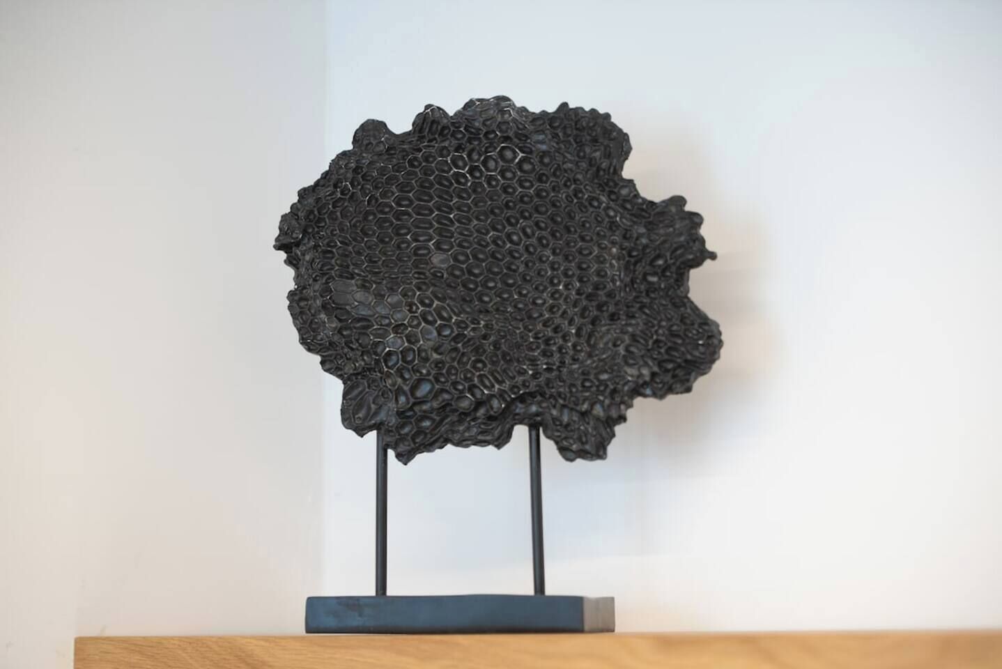 Une sculpture à la surface texturée, placée sur un socle devant un fond uni.