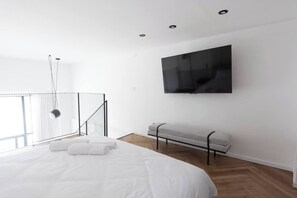 A modern bedroom with a large bed, a bench, a TV mounted on the wall, and a balcony with a railing. - Port city haifa-Urbanic Loft heart of haifa Dwntwn (Haifa)