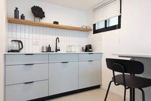A modern kitchen with a white tiled backsplash, a wooden shelf, and a black chair. - Port city haifa-Urbanic Loft heart of haifa Dwntwn (Haifa)