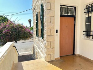 Un edificio con facciata in pietra, una porta in legno e una finestra con inferriata metallica.