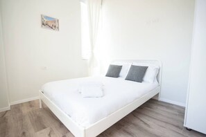 Une chambre avec un lit simple, une tête de lit blanche, des oreillers gris et un lit bien fait avec du linge de lit blanc.
