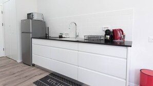 Een moderne keuken met witte kastjes, een zwart aanrecht, een roestvrijstalen koelkast, een spoelbak en een waterkoker.