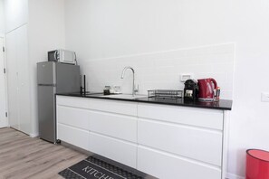A modern kitchen with white cabinets, a black countertop, a stainless steel refrigerator, a sink, and a kettle. - Port city haifa authentic 2bdrmsblcny germancolony (Haifa)