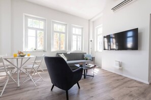 A modern living room with a sofa, a dining table with chairs, and a flat-screen TV mounted on the wall. - Port city haifa authentic 2bdrmsblcny germancolony (Haifa)