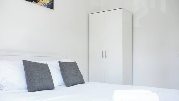 Een hotelkamer met een bed, twee kussens, een kledingkast en een schilderij aan de muur.