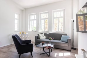 A modern living room with a grey sofa, a black armchair, and a coffee table with a book and flowers. - Port city haifa authentic 2bdrmsblcny germancolony (Haifa)