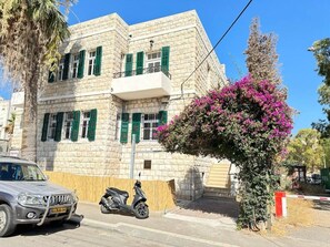 A stone building with a balcony, a parked scooter, and a vehicle in front. - Port city haifa authentic 2bdrmsblcny germancolony (Haifa)