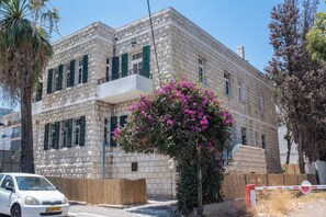 A multi-story building with a stone facade, a balcony, and a car parked in front.