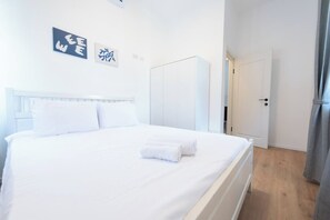 A hotel room with a bed, white walls, a wardrobe, and a door leading to another room. - Port city haifa - authentic 2 bdrms germancolony 2 (Haifa)