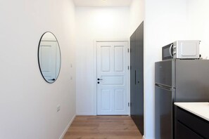 A hallway with a white door, a mirror, and a kitchenette area with a microwave and refrigerator.