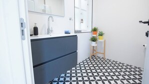 A modern bathroom with a black and white patterned floor, a large mirror, a sink with a faucet, and a small plant on a shelf. - Port city haifa - authentic 2 bdrms germancolony 3 (Haifa)