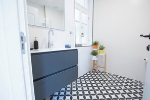 Une salle de bain moderne avec un carrelage noir et blanc à motifs, un grand miroir, un lavabo avec un robinet et une petite plante posée sur une étagère.