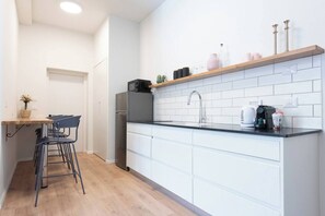 A modern kitchen with white cabinetry, a black countertop, and a wooden shelf above the sink. - Haifa German Colony 2BR Apt, Sleeps 5 (Haifa)